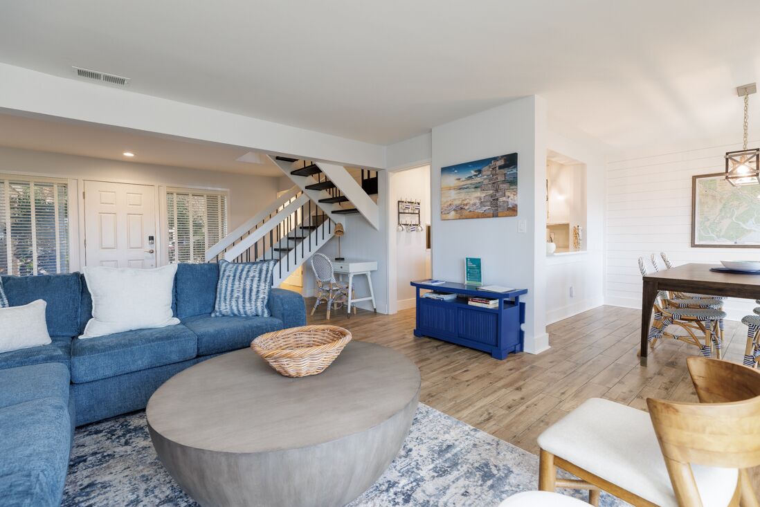 Un salon moderne avec un canapé bleu, une table basse ronde et un escalier menant à l’étage supérieur.