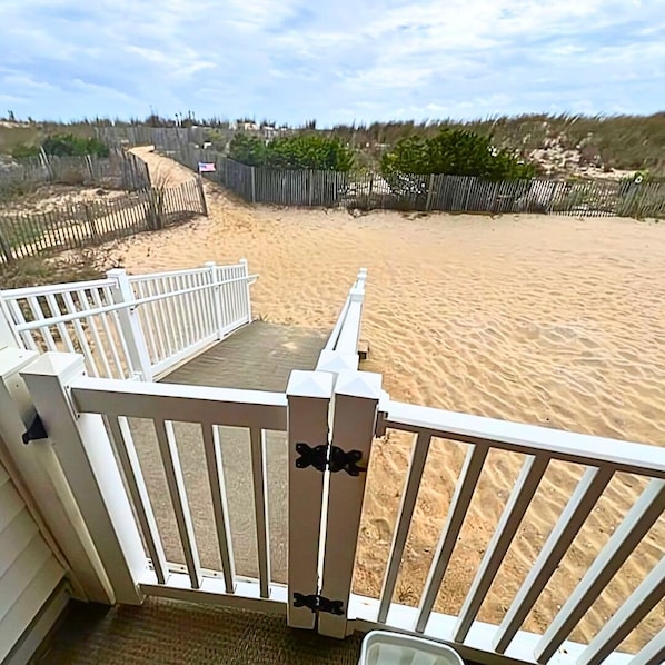 Vista da praia a partir de um deck com guarda-corpo branco, praia de areia e uma cerca ao fundo.