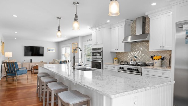 A modern kitchen with white cabinetry, a large island with bar stools, stainless steel appliances, and pendant lighting. - Historic Sea Captain's Home in Downtown Chatham (Chatham)