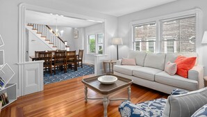 A living room with a sofa, a coffee table, and a dining area with chairs and a staircase. - Historic Sea Captain's Home in Downtown Chatham (Chatham)