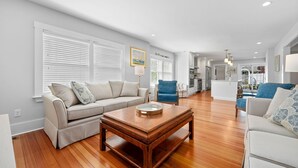 A spacious living room with a wooden coffee table, a beige sofa, and a blue armchair. - Historic Sea Captain's Home in Downtown Chatham (Chatham)