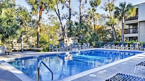 A swimming pool with lounge chairs, palm trees, and a small building in the background. - Steps to Beach, Coligny Plaza: Hilton Head Condo! (Hilton Head Island)