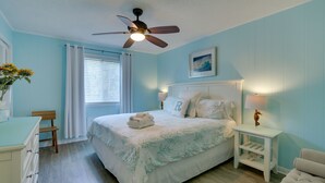 A bedroom with a bed, a nightstand, a chair, a desk, a ceiling fan, and a window with curtains. - Steps to Beach, Coligny Plaza: Hilton Head Condo! (Hilton Head Island)
