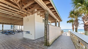 Terraza de madera al aire libre con mesas de picnic y vista a la playa.