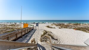Una playa con un paseo marítimo de madera que lleva al agua, dunas de arena y sombrillas a lo largo de la orilla.
