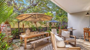 Un patio al aire libre con una mesa de madera, bancos y una zona de estar con cojines.