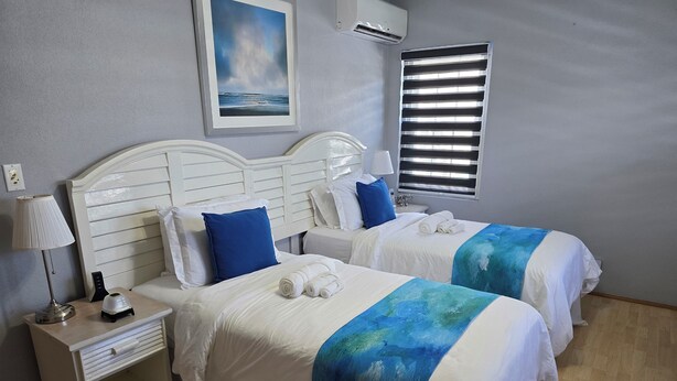 Une chambre d’hôtel avec deux lits, des têtes de lit blanches et un tableau représentant une scène de plage.