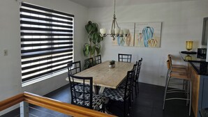 Un coin repas avec une table en bois, des chaises à motifs noir et blanc, une plante en pot et un lustre.