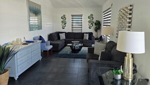 Un salon moderne avec un canapé d’angle, une table basse et un coin repas agrémenté d’une commode blanche.