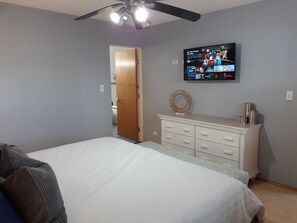A bedroom with a bed, a dresser, a television on the wall, and a ceiling fan.