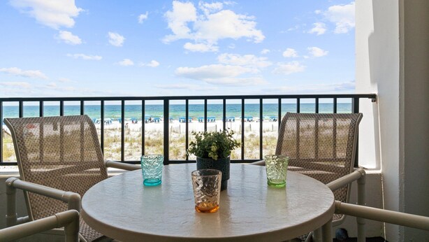 Un balcon avec deux fauteuils en osier, une petite table et un pot de fleurs. La vue comprend une plage et l’océan.