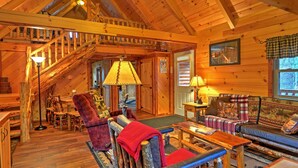 A log cabin interior with a staircase, wooden furniture, and a cozy fireplace. - Rustic Dundee Log Cabin w/ Hot Tub & Forest Views! (Dundee)