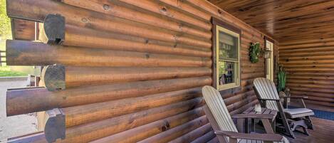 A log cabin with a wooden deck, two Adirondack chairs, and a window with a wreath.