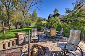 An outdoor patio with stone seating, a fire pit, and a view of a house in the background. - Rustic Dundee Log Cabin w/ Hot Tub & Forest Views! (Dundee)