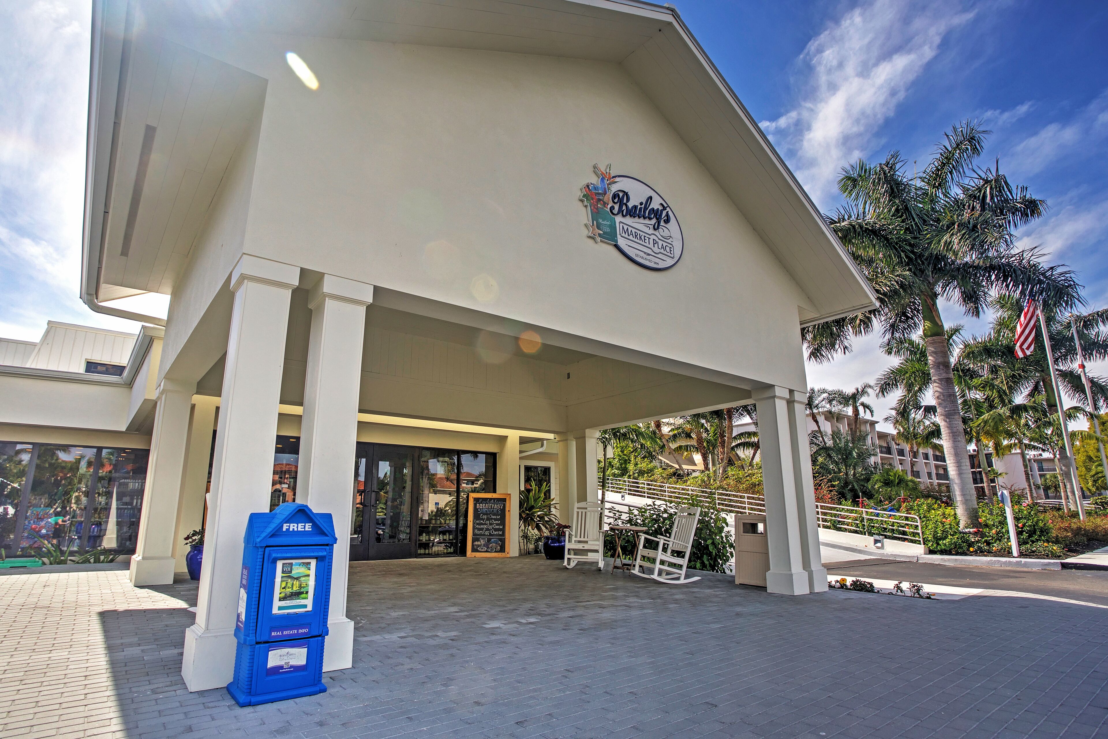 Een Bailey's Market Place met een blauwe brievenbus, witte zuilen en palmbomen.