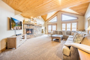 A spacious living room with a stone fireplace, a large sofa, and a television on a wooden cabinet. - Lowell 1175 (Park City)