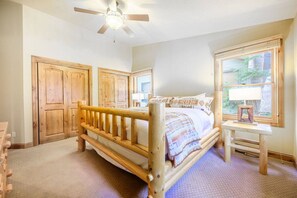 A bedroom with a wooden bed, a ceiling fan, a window with a view, and a wooden dresser.