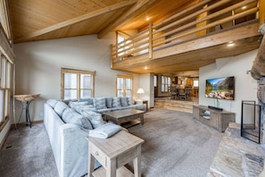 A spacious living room with a high ceiling, a built-in staircase, a large sofa, a coffee table, and a television. - Lowell 1175 (Park City)