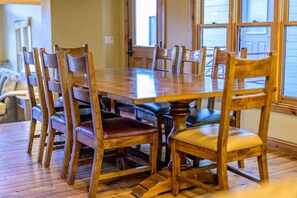 Una mesa de comedor con sillas de madera, piso de madera y ventanas con persianas.