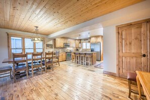 A spacious kitchen with wooden cabinets, a central island with stools, and a dining area with a wooden table and chairs. - Lowell 1175 (Park City)