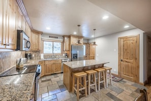 A kitchen with wooden cabinets, granite countertops, a stainless steel refrigerator, and a bar stool area.