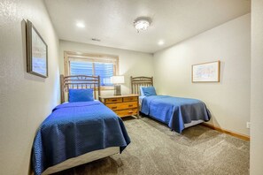 Un dormitorio con dos camas individuales, una mesita de noche, un aparador y una ventana con persianas.