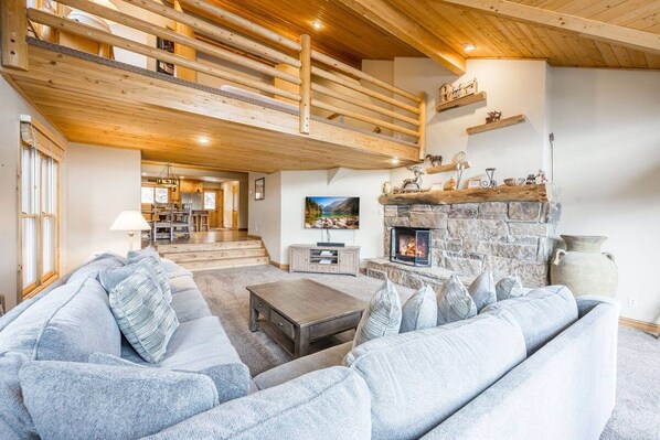 A cozy living room with a stone fireplace, a wooden staircase, and a sofa set. - Lowell 1175 (Park City)