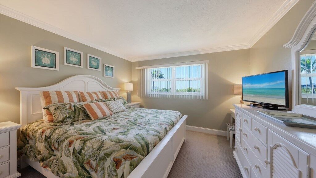 A bedroom with a bed, a television, a dresser, and framed pictures on the wall.