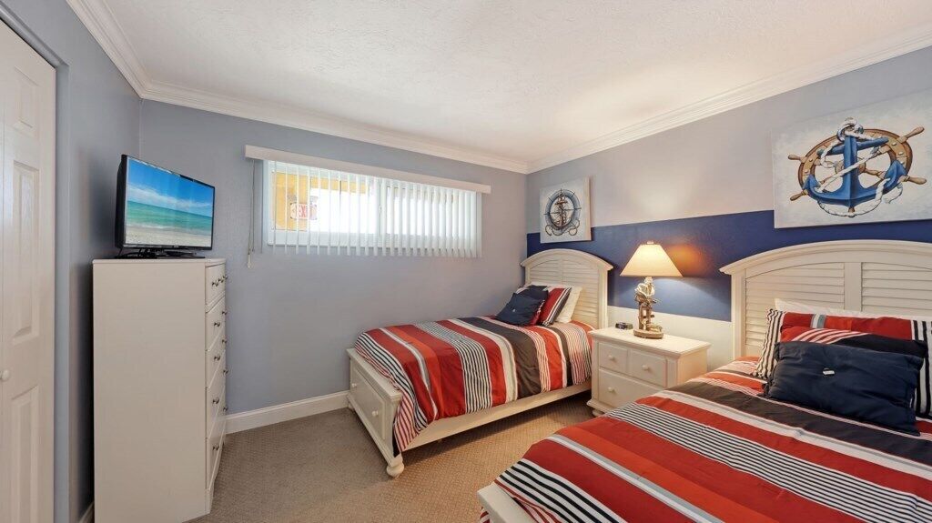 A bedroom with two beds, a television, a nightstand with a lamp, and nautical-themed decor.
