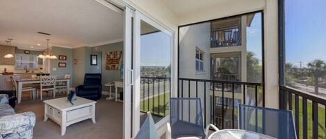 En balkon med udsigt til en bygning, et spiseområde med bord og stole, og en opholdsstue med sofa og sofabord.