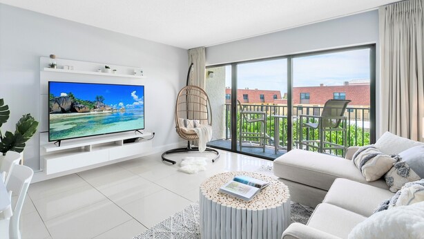 Ein modernes Wohnzimmer mit Flachbildfernseher, einem Korbstuhl, einer Couch und einem Balkon mit Blick auf Gebäude und Grünflächen.