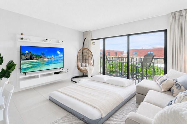 Une chambre moderne dotée d’une grande télévision, d’un lit, d’un balcon offrant une vue sur les immeubles et d’un fauteuil suspendu.
