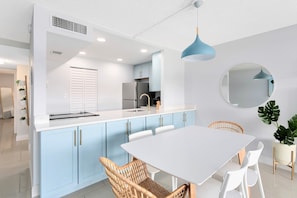 A modern kitchen with light blue cabinets, a white countertop, and a round mirror on the wall.