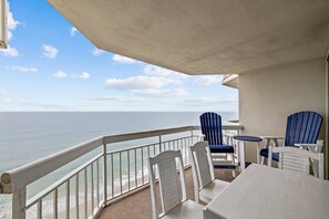 Un balcone con vista sull'oceano, con sedie bianche e un tavolino.