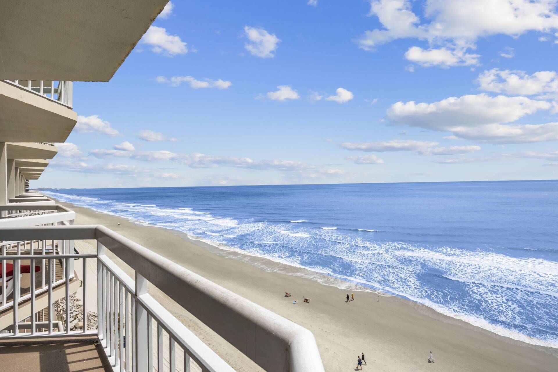Vista a la playa desde un balcón, con cielo despejado y olas marinas.