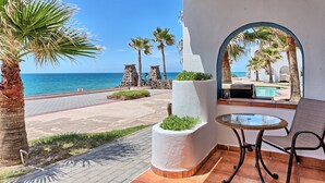 A patio with a glass table and chair, a view of the sea, and a pool area.