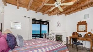 A bedroom with a bed, a desk, and a view of the sea.
