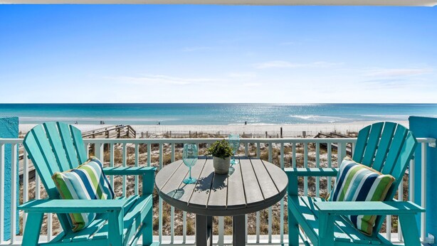 Una terraza con dos sillas Adirondack turquesa y una mesa redonda con una planta en maceta, con vista a una playa.