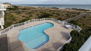 A swimming pool with a unique shape, surrounded by a white fence, overlooking a beach and ocean. - Beautiful oceanfront condo in Ocean Dunes! (Wrightsville Beach)
