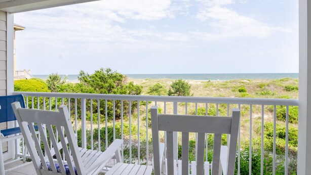 A covered porch with white railings and two white chairs, overlooking a beach with sand dunes and the ocean. - Beautiful oceanfront condo in Ocean Dunes! (Wrightsville Beach)
