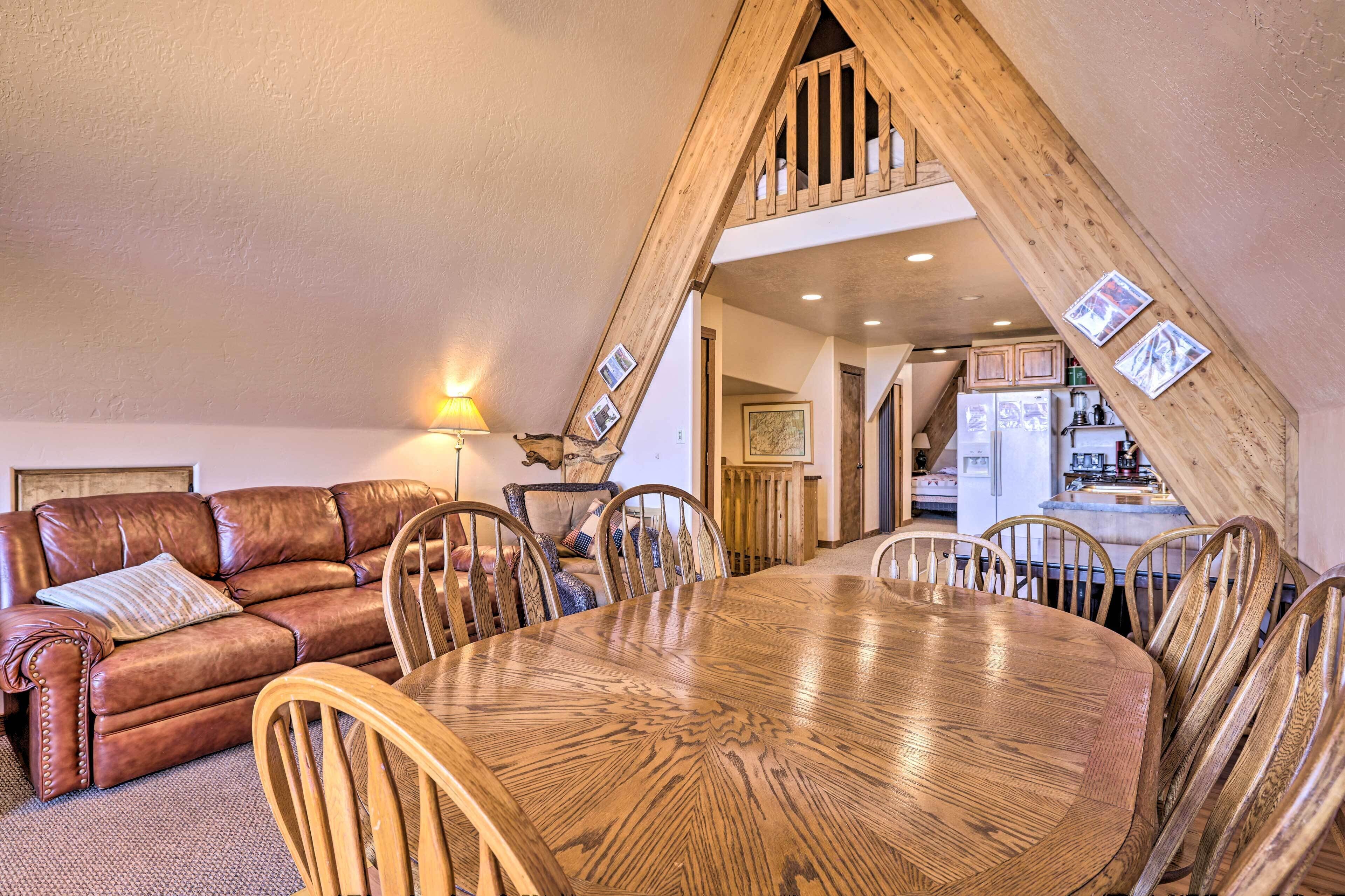 Un salón acogedor con un sofá de cuero marrón, una mesa de comedor de madera y sillas. Una escalera conduce a un nivel superior.