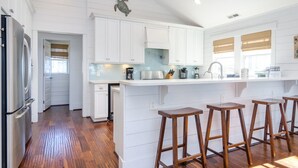 Una cocina amplia con armarios blancos, una isla central con taburetes y un refrigerador grande.