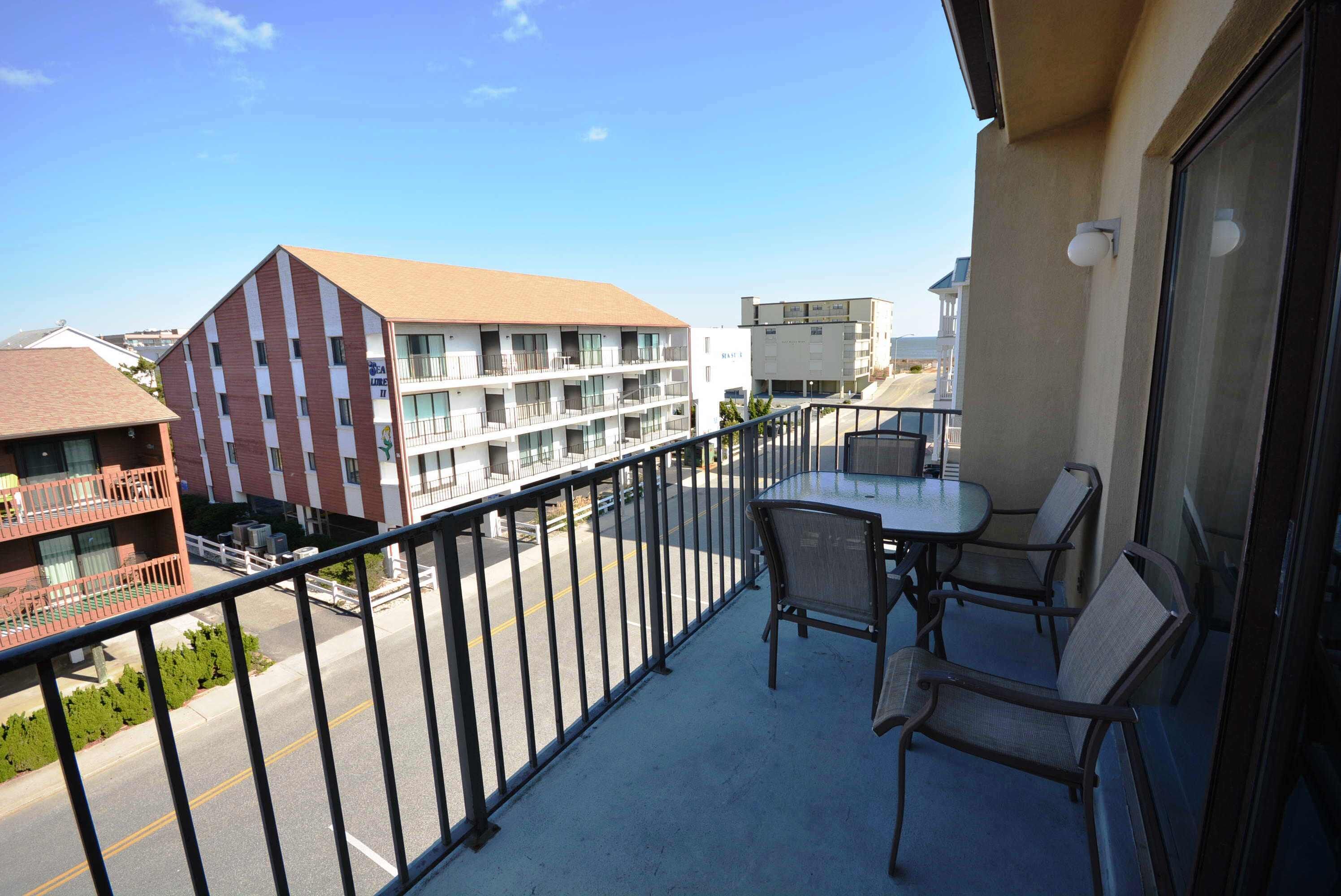 A balcony with a table and chairs, overlooking a street with buildings and a clear sky.