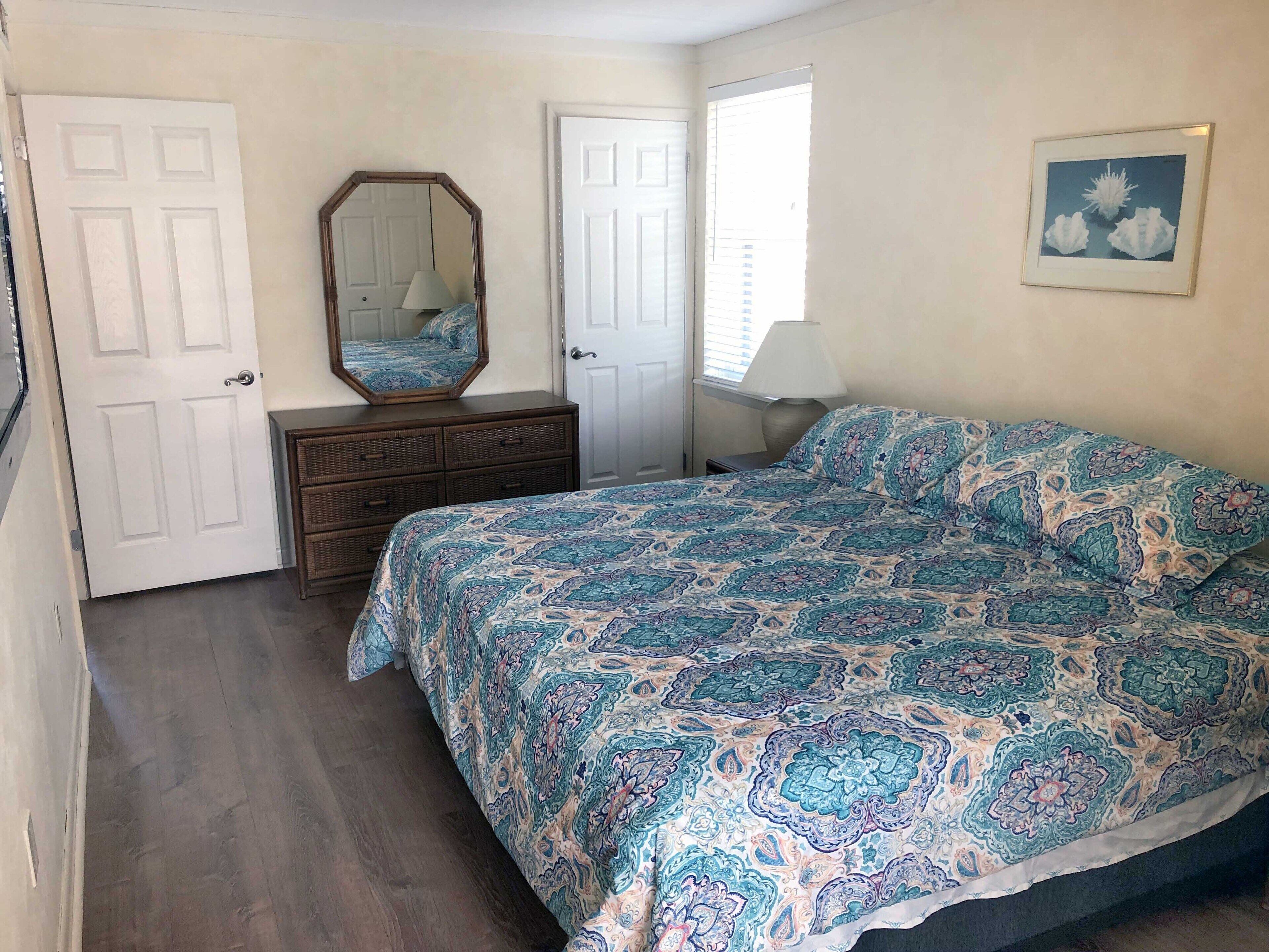 A bedroom with a bed, dresser, mirror, and doors.