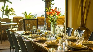 A dining table set for a meal with chairs, a vase with flowers, and a view of the ocean. - 2 FREE NIGHTS IN CABO at Casa Maravilla! (Palmilla)