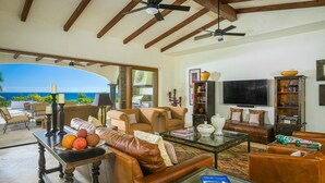 A spacious living room with leather sofas, a coffee table, and a television. There is a bookshelf and a large window offering a view of the ocean. - 2 FREE NIGHTS IN CABO at Casa Maravilla! (Palmilla)