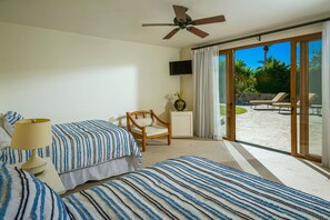 A bedroom with two beds, a ceiling fan, a TV, and a view of a patio with a chair and a table. - 2 FREE NIGHTS IN CABO at Casa Maravilla! (Palmilla)