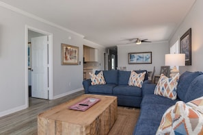 A living room with a blue sofa set, a wooden coffee table, and a ceiling fan. - Oceanfront 3 Bedroom Penthouse with a Pool! (Carolina Beach)