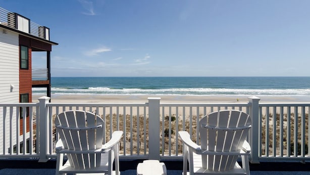 A balcony with white chairs overlooking a beach.