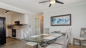 A modern kitchen with white cabinetry, a glass dining table, and a ceiling fan.